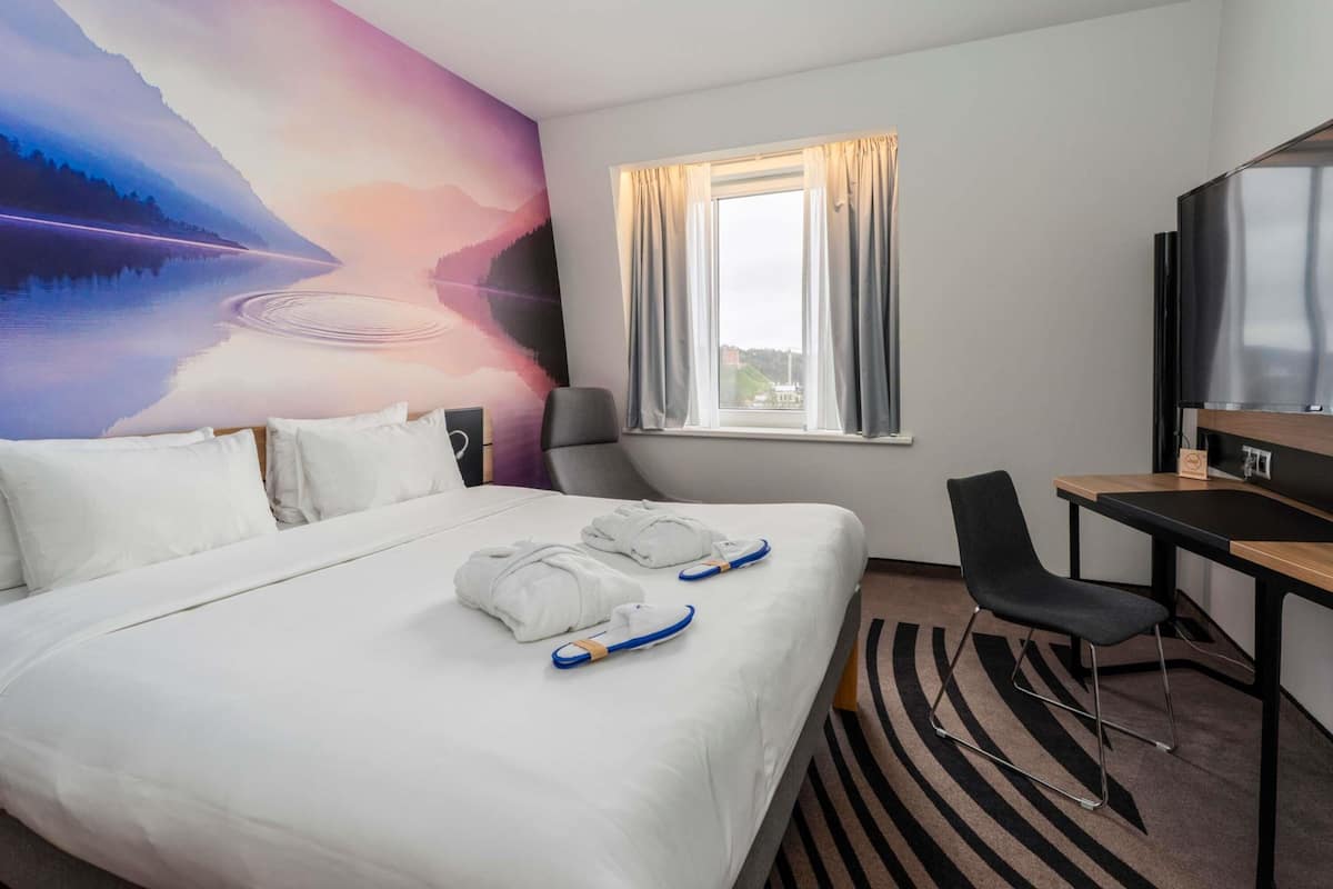 A hotel room with a bed, a desk, a chair, a TV, and a large wall mural.