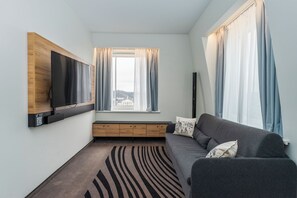 Una sala de estar moderna con un televisor de pantalla plana montado en un panel de madera, un sofá gris con cojines, una ventana con cortinas y una alfombra estampada.