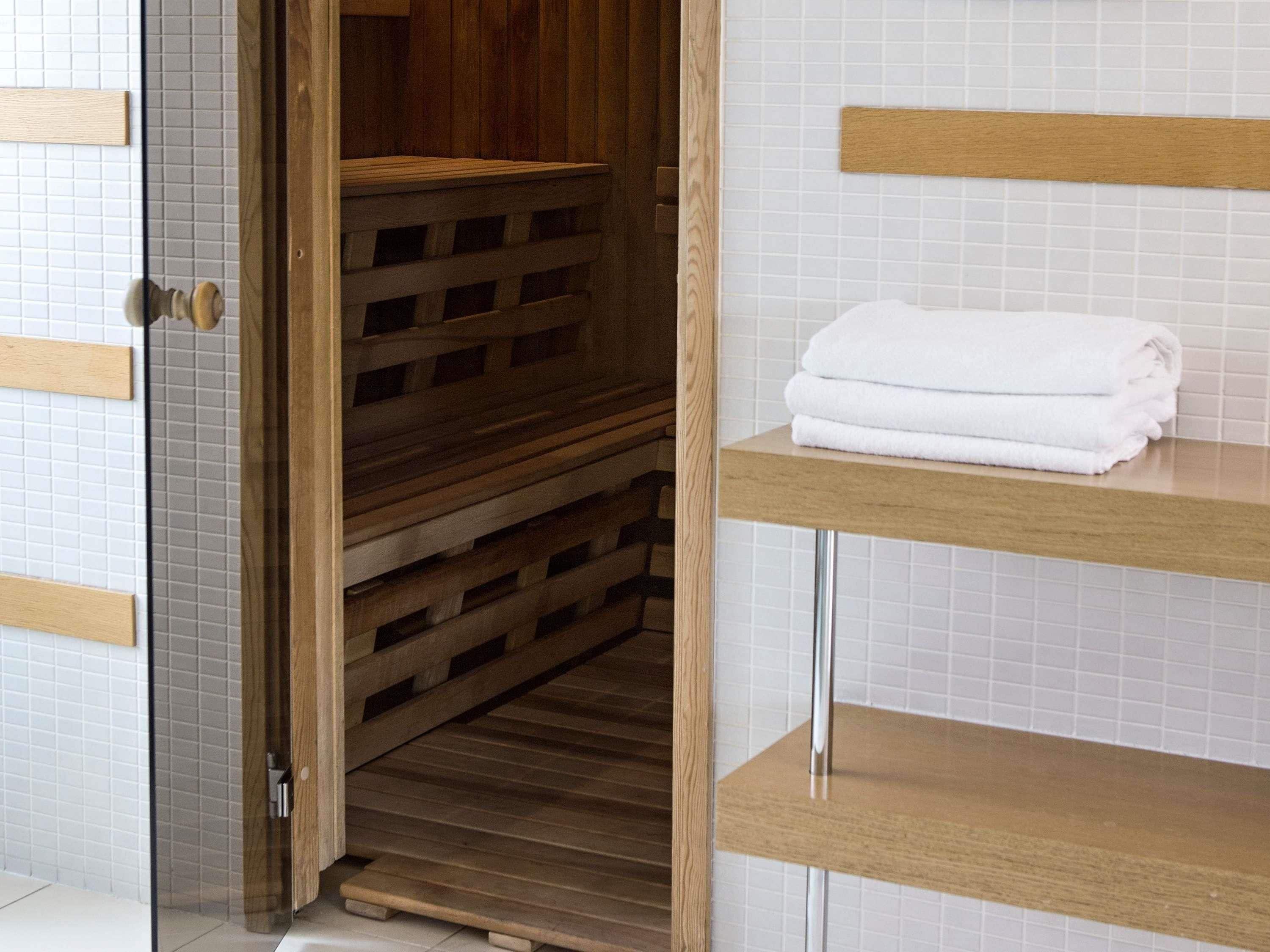 A wooden sauna with a bench, a wooden door, and a white tiled wall.