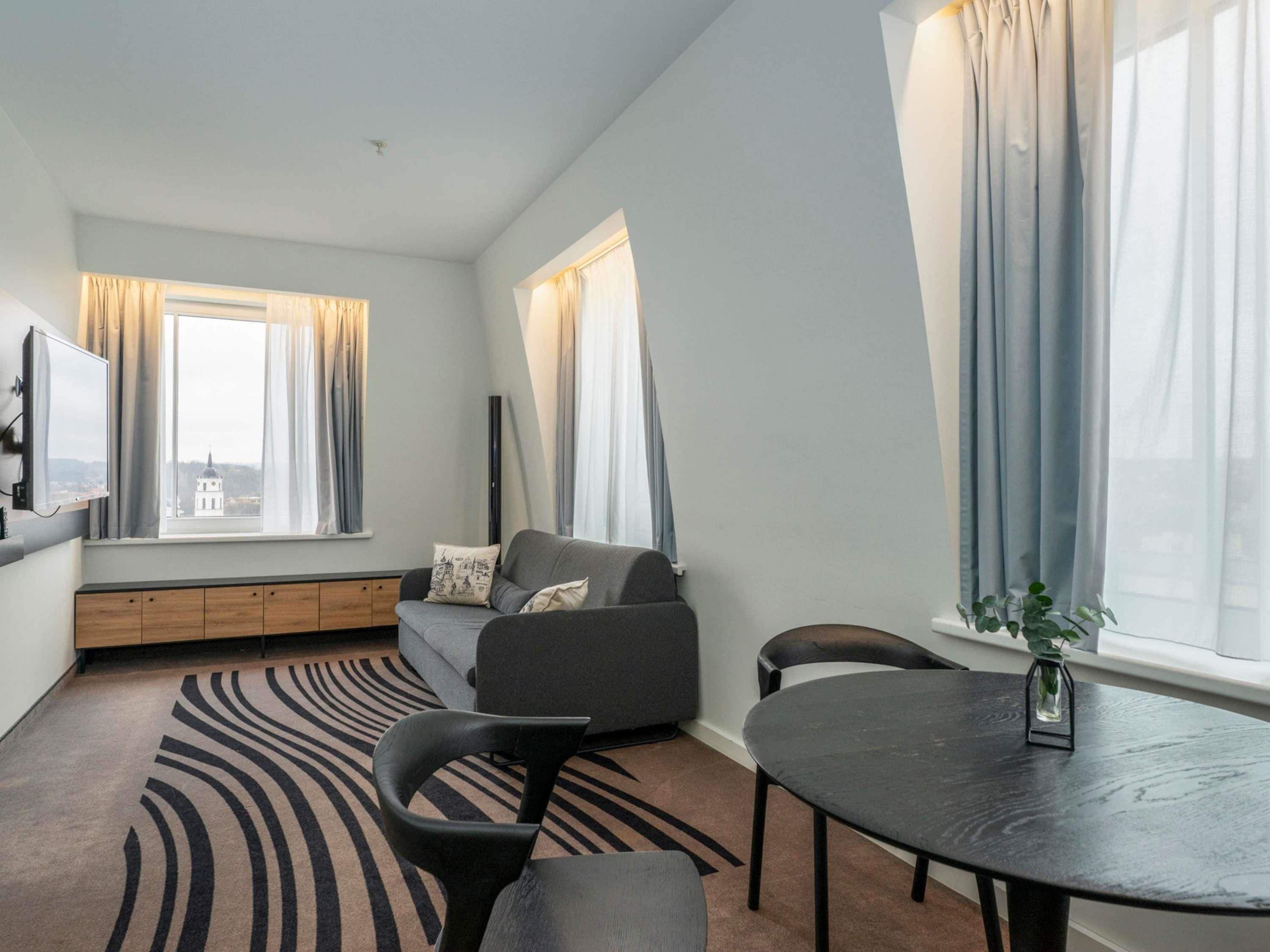 Una sala moderna con un sofá, una mesa de comedor y vistas a un edificio a través del ventanal.