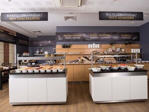 A buffet area with labeled sections for hot dishes, cold starters, juices, water, bakery, pastries, and cereals. - Novotel Vilnius Centre (Vilnius)