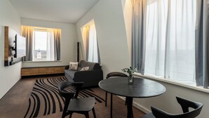 A modern living room with a sofa, chairs, a TV, and a dining table. - Novotel Vilnius Centre (Vilnius)
