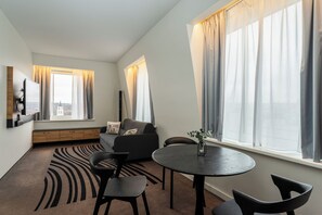 A modern living room with a sofa, chairs, a TV, and a dining table. - Novotel Vilnius Centre (Vilnius)