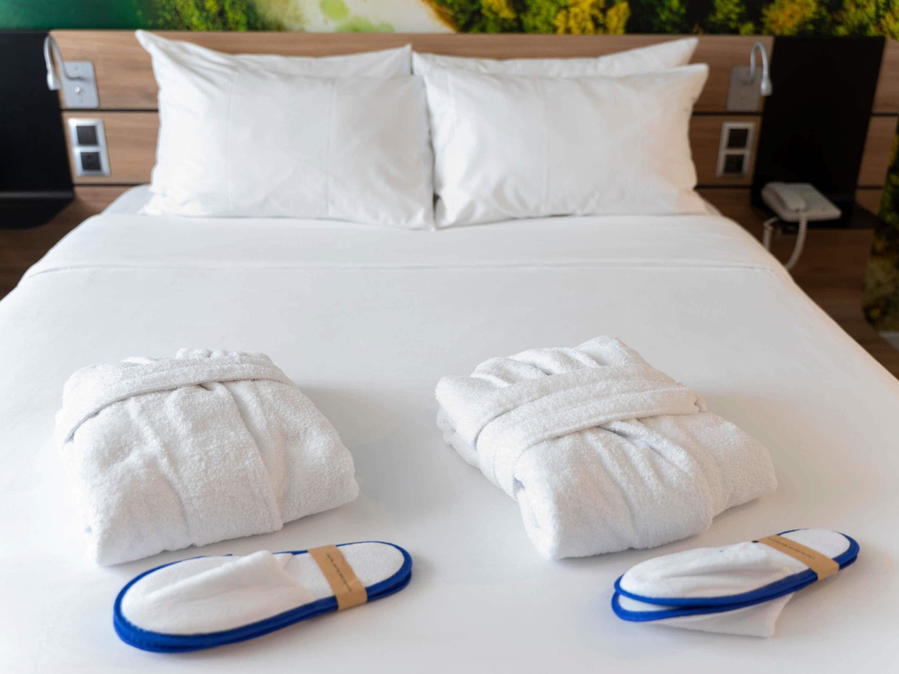 A neatly made bed with white bedding, two towels, and slippers.