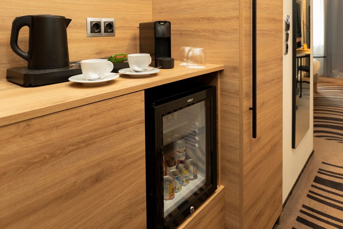 A compact kitchenette with a coffee maker, a kettle, a glass, and a mini-fridge.