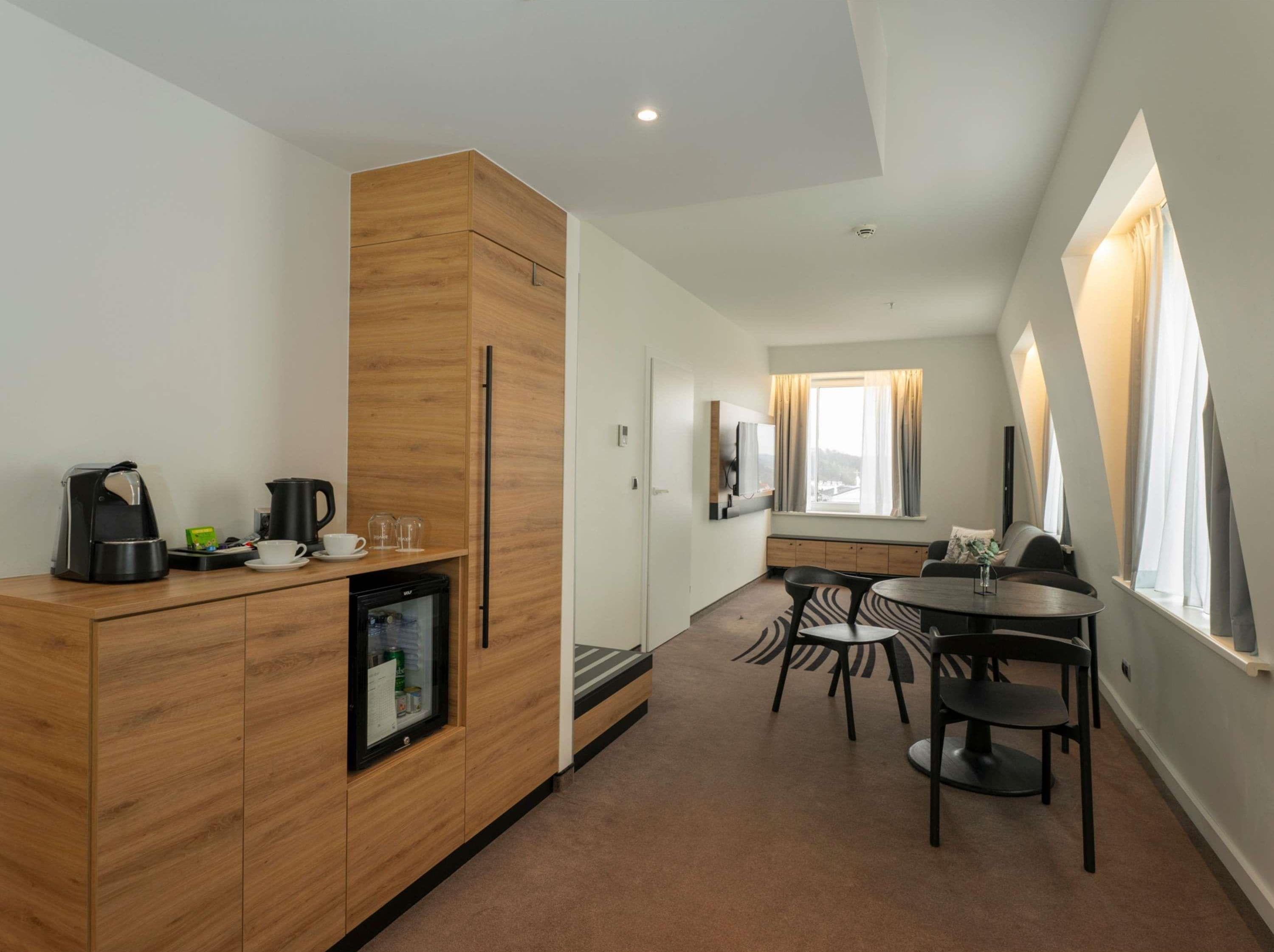 Eine moderne Küche mit Kaffeemaschine, Wasserkocher und Kühlschrank, ein Essbereich mit Tisch und Stühlen sowie ein großes Fenster mit Vorhängen.