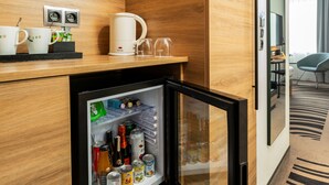 A hotel minibar with a refrigerator stocked with beverages and snacks, a coffee machine, and two cups on the counter. - Novotel Vilnius Centre (Vilnius)