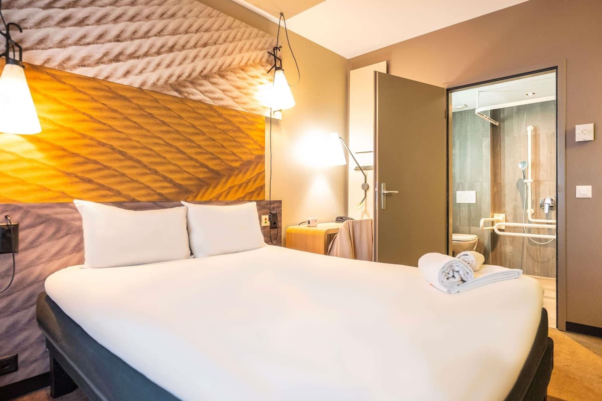 Ein Hotelzimmer mit einem großen Bett, einem Nachttisch, einer Lampe und einer Duschkabine.