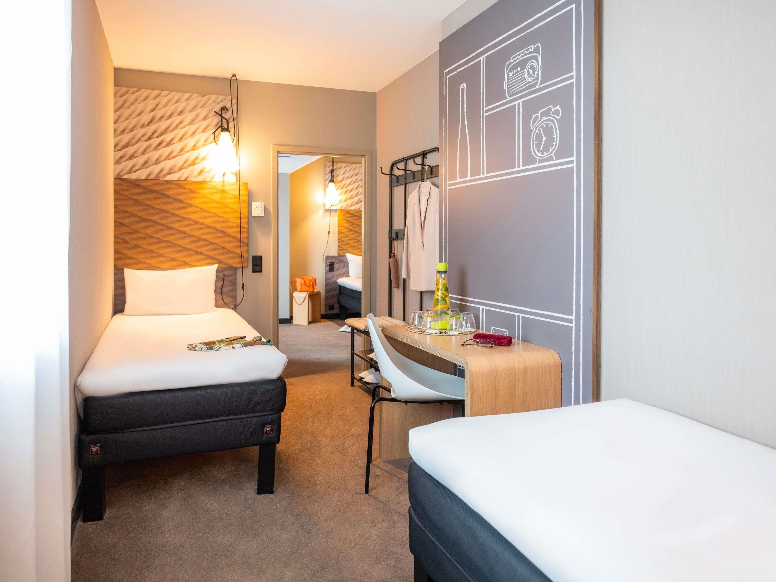 A hotel room with two beds, a desk, a mirror, and a wall with a chalkboard design.