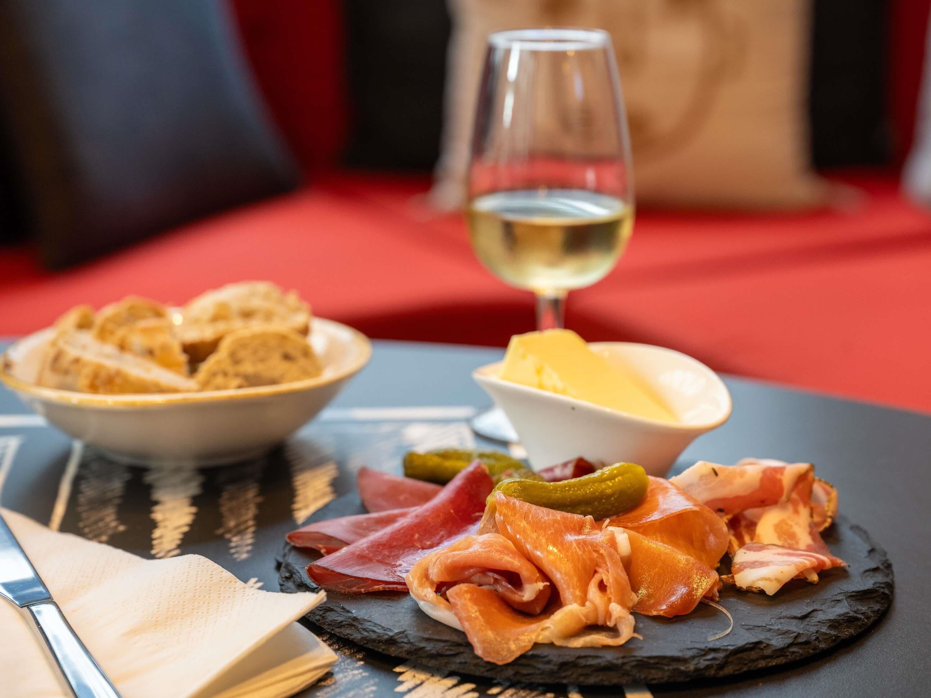 A table with a cheese board, a bowl of bread, a glass of white wine, and a plate of cured meats.