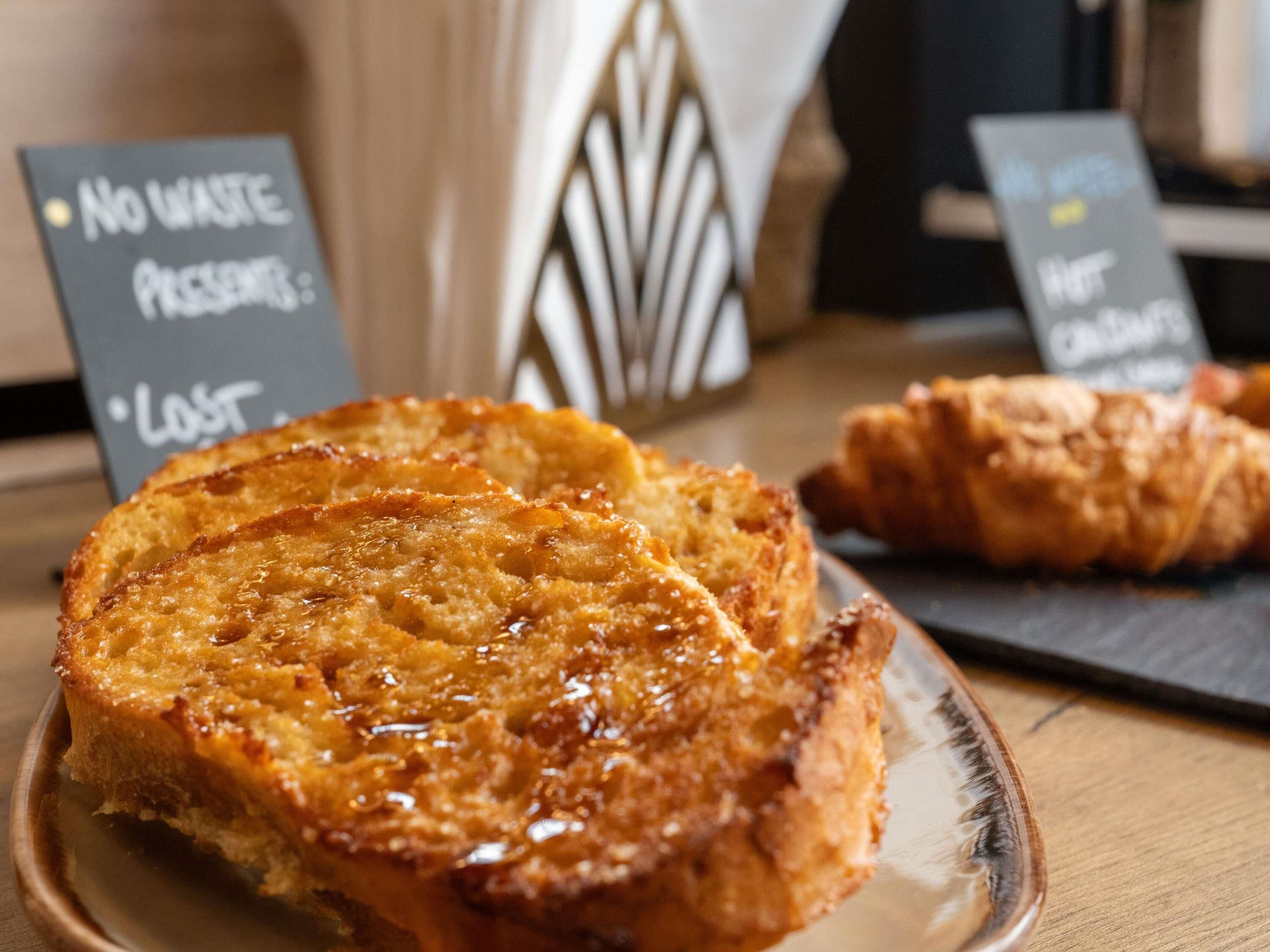 A plate of French toast with syrup, a croissant, and a sign indicating no waste present.