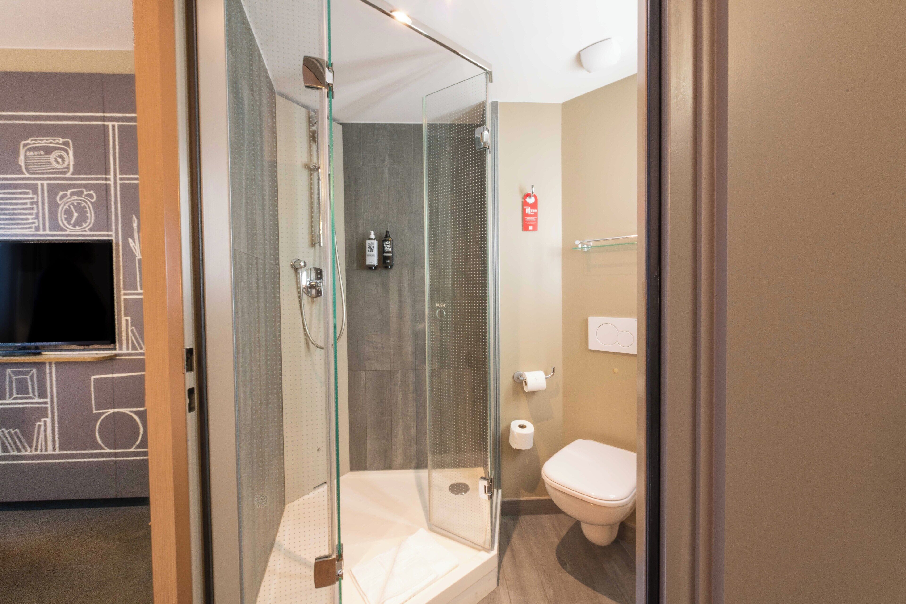Une salle de bain moderne dotée d’une douche à parois de verre, de toilettes et d’un lavabo.