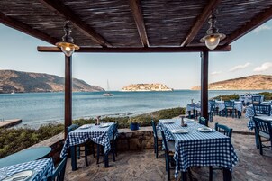 An outdoor dining area with checkered tablecloths and chairs, overlooking a body of water with a distant island.