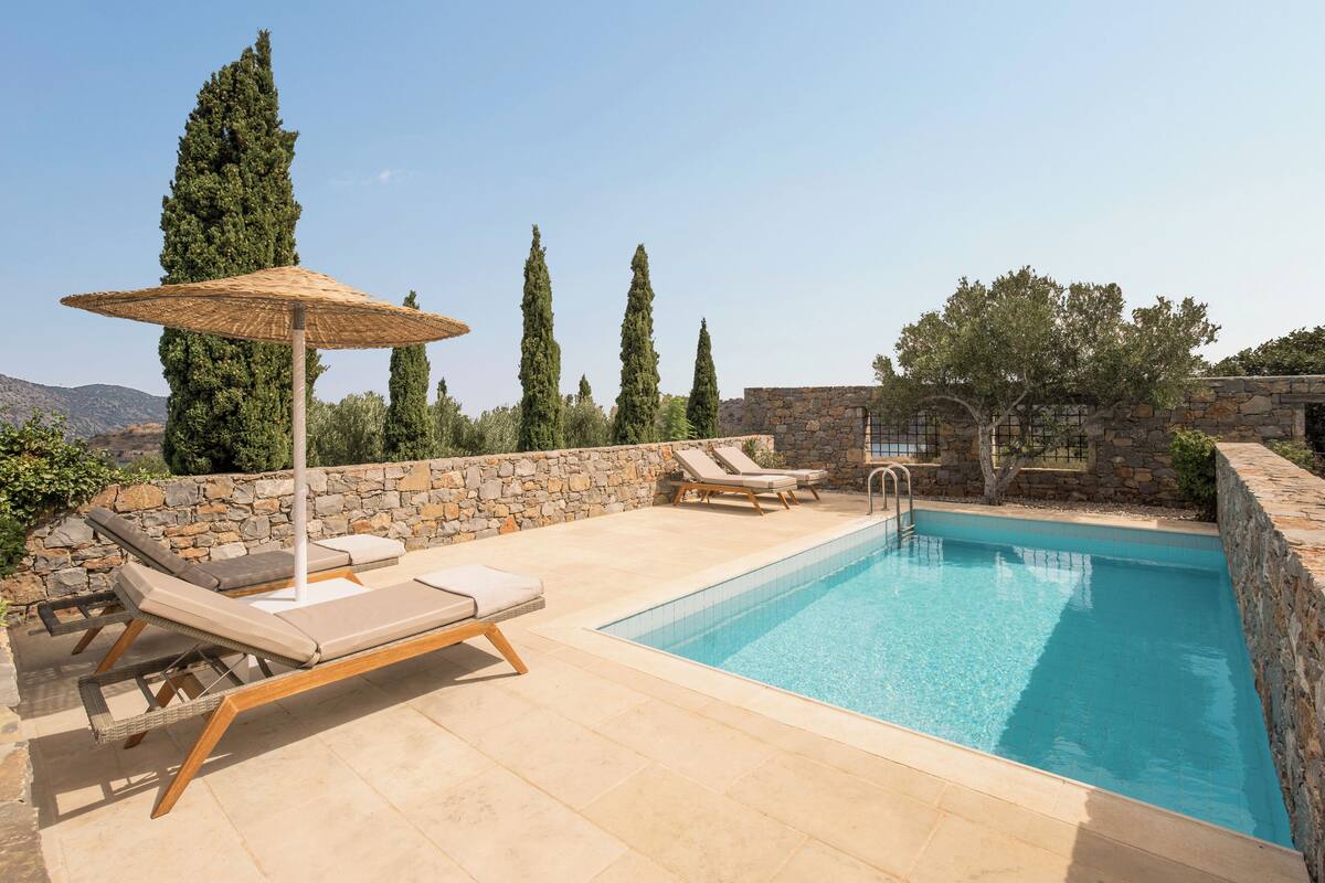 A pool with lounge chairs and a stone wall.