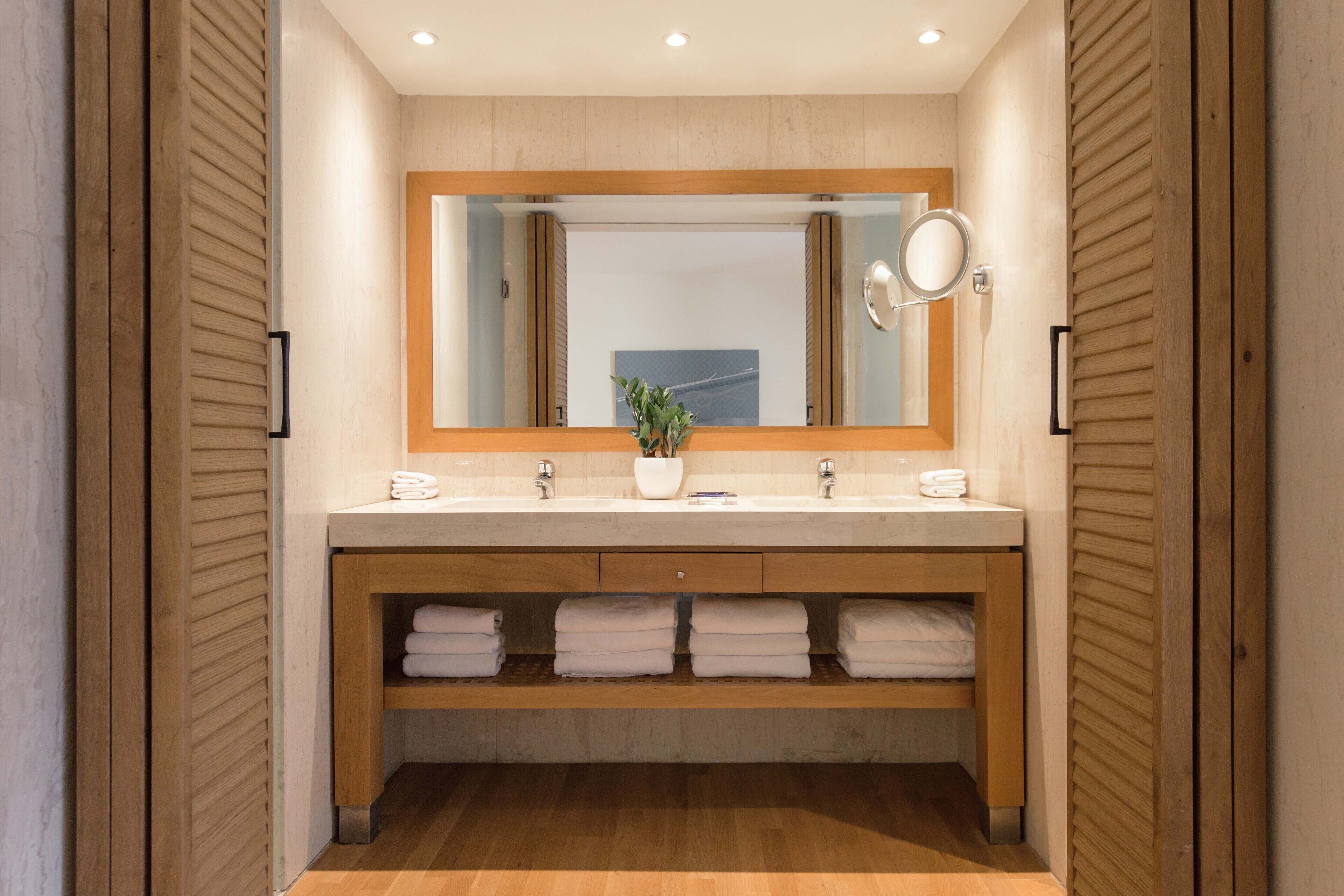 Un baño moderno con tocador de madera, dos lavamanos, un espejo y un estante con toallas dobladas.