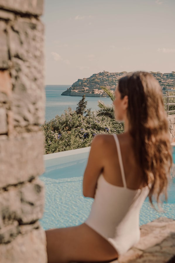 Una persona sentada junto a una piscina con vistas a un paisaje costero.