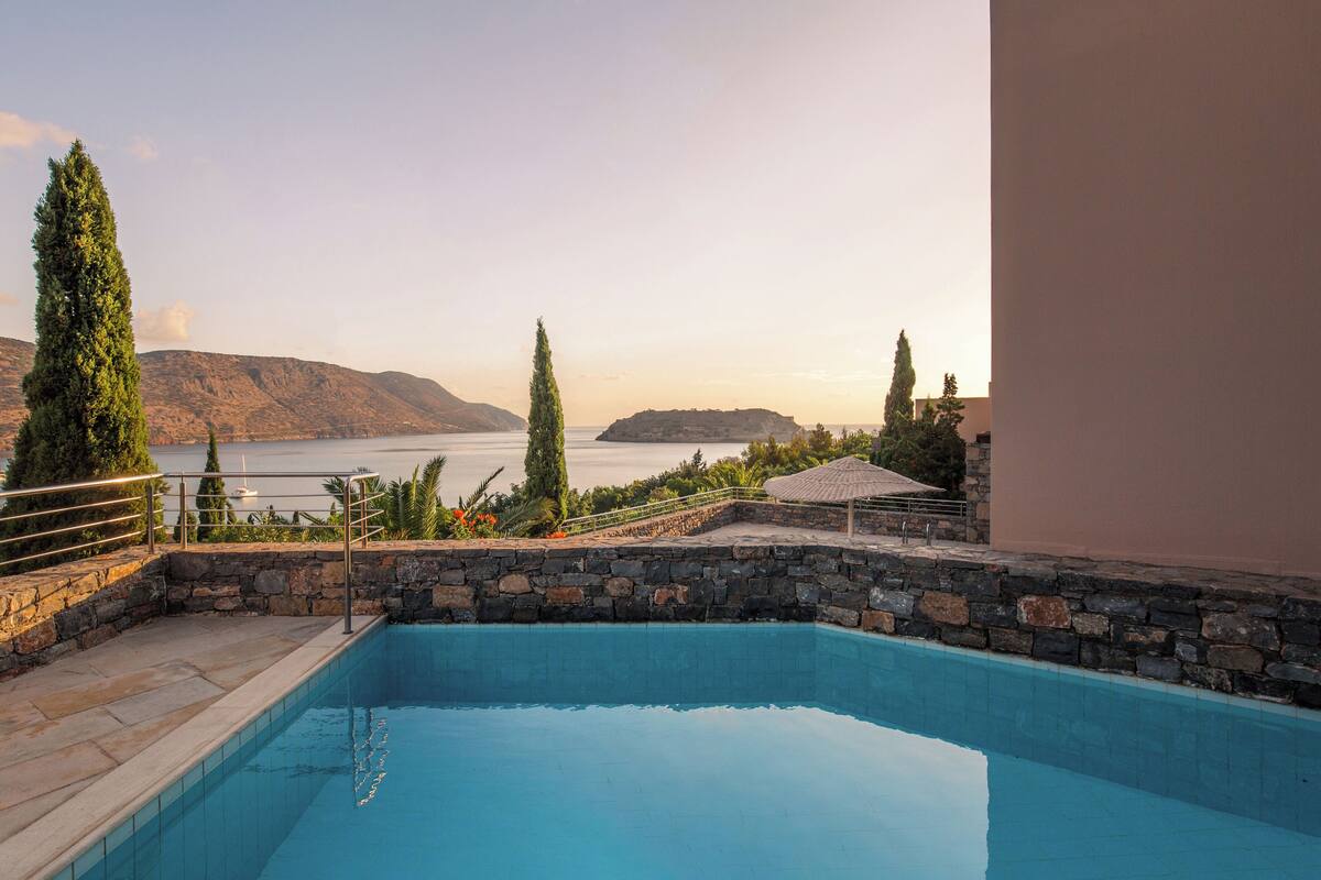 A swimming pool with a stone border, a view of a lake, and distant mountains.