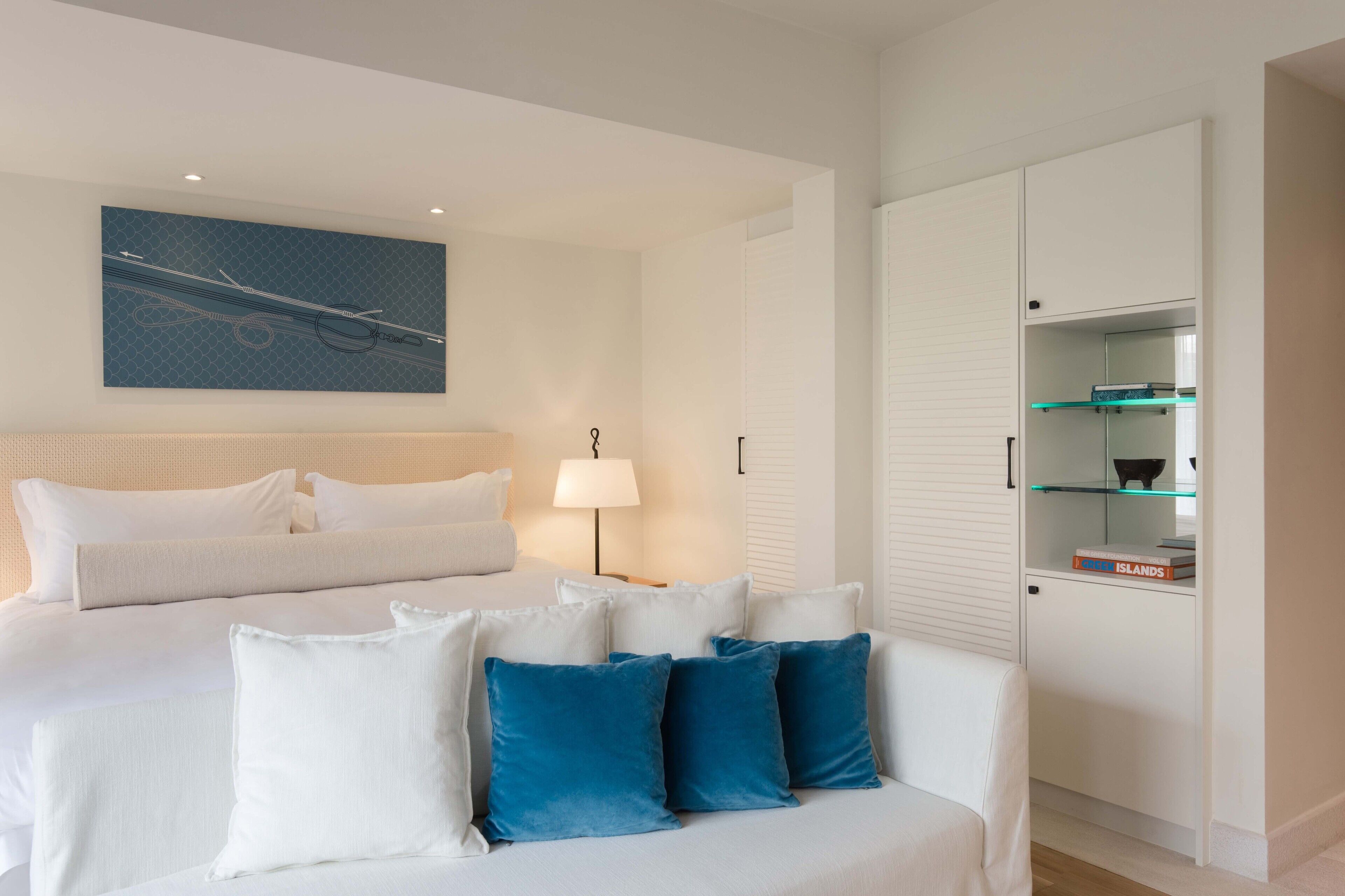 Una habitación de hotel moderna con una cama, un sofá blanco, una mesita de noche, una lámpara y un armario.