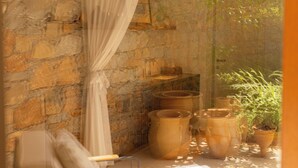 A room with a stone wall, a white curtain, a white chair, and several potted plants.