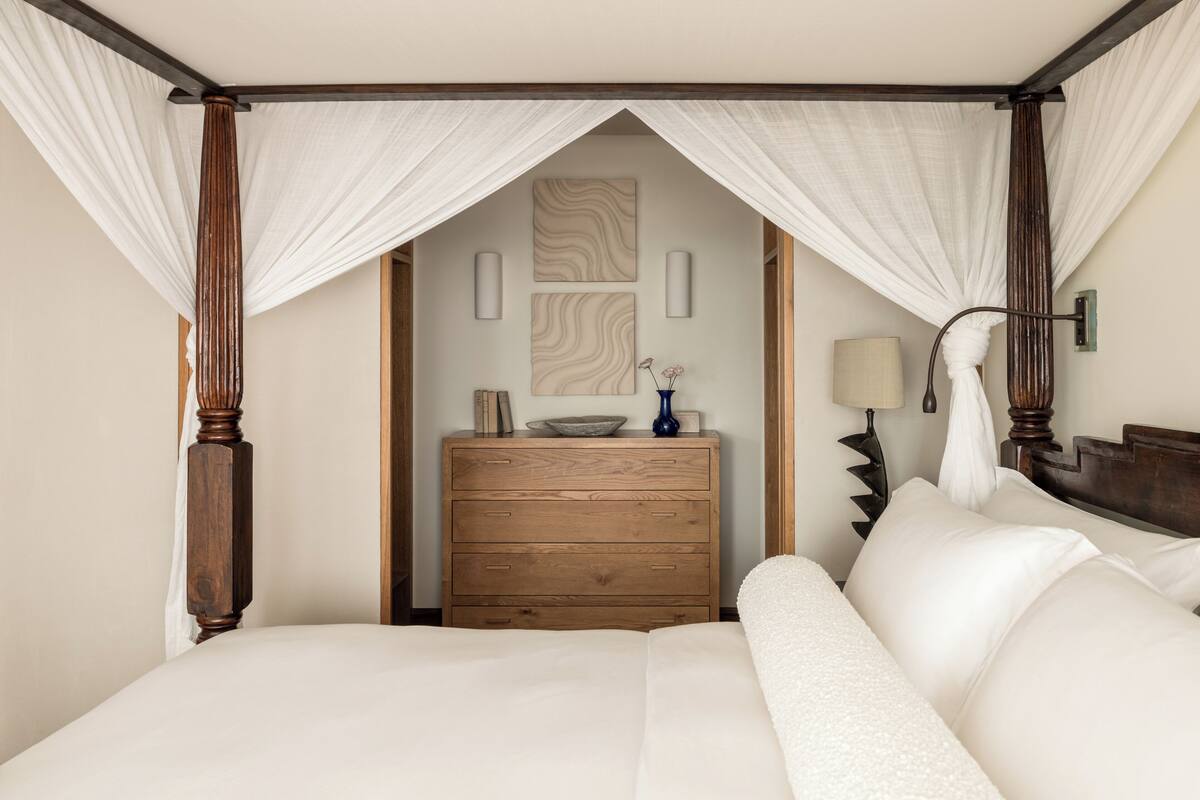 A bedroom with a canopy bed, wooden dresser, and a wall-mounted lamp.