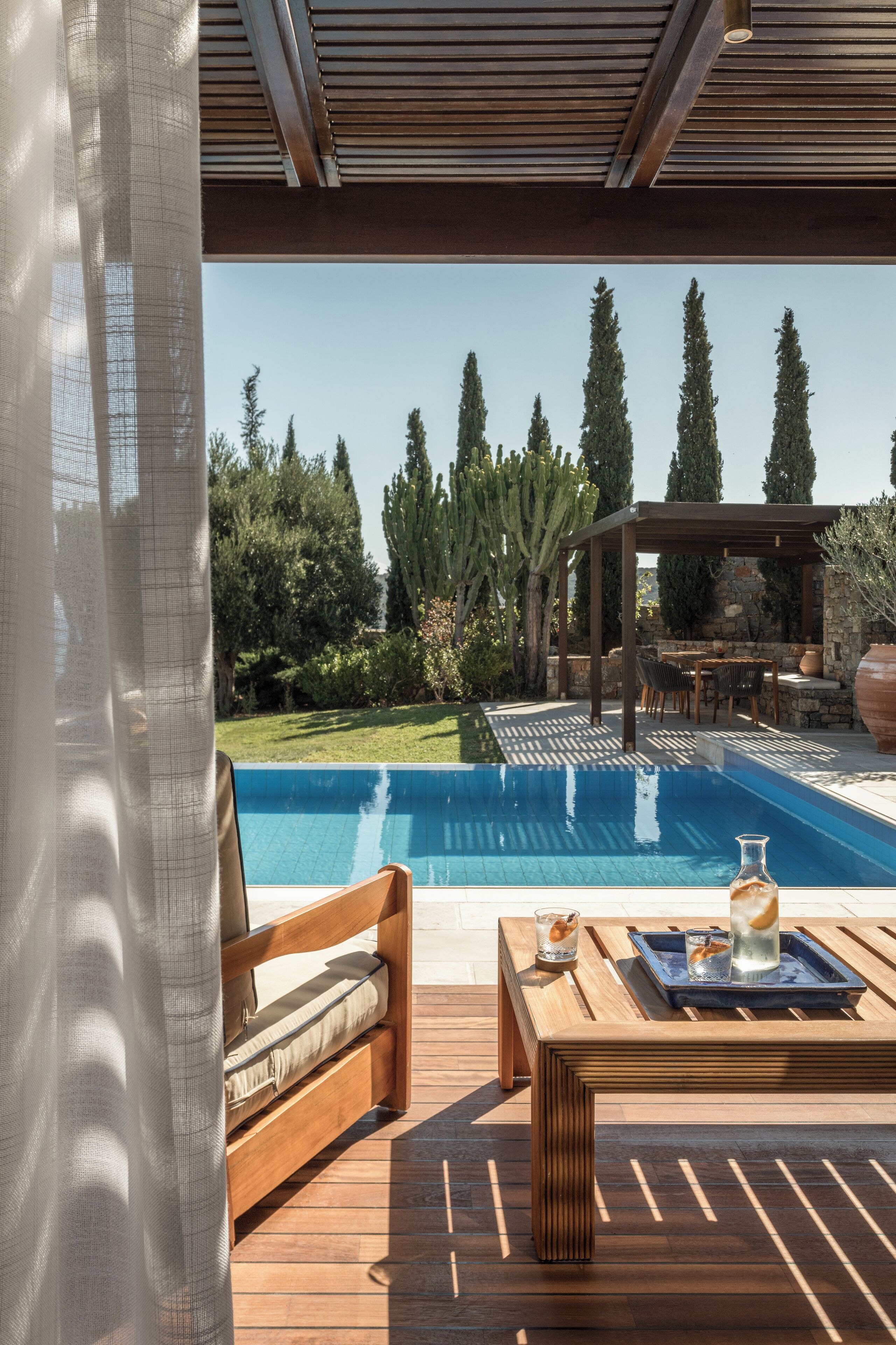 Una terraza de madera con piscina, mobiliario exterior y una pérgola.