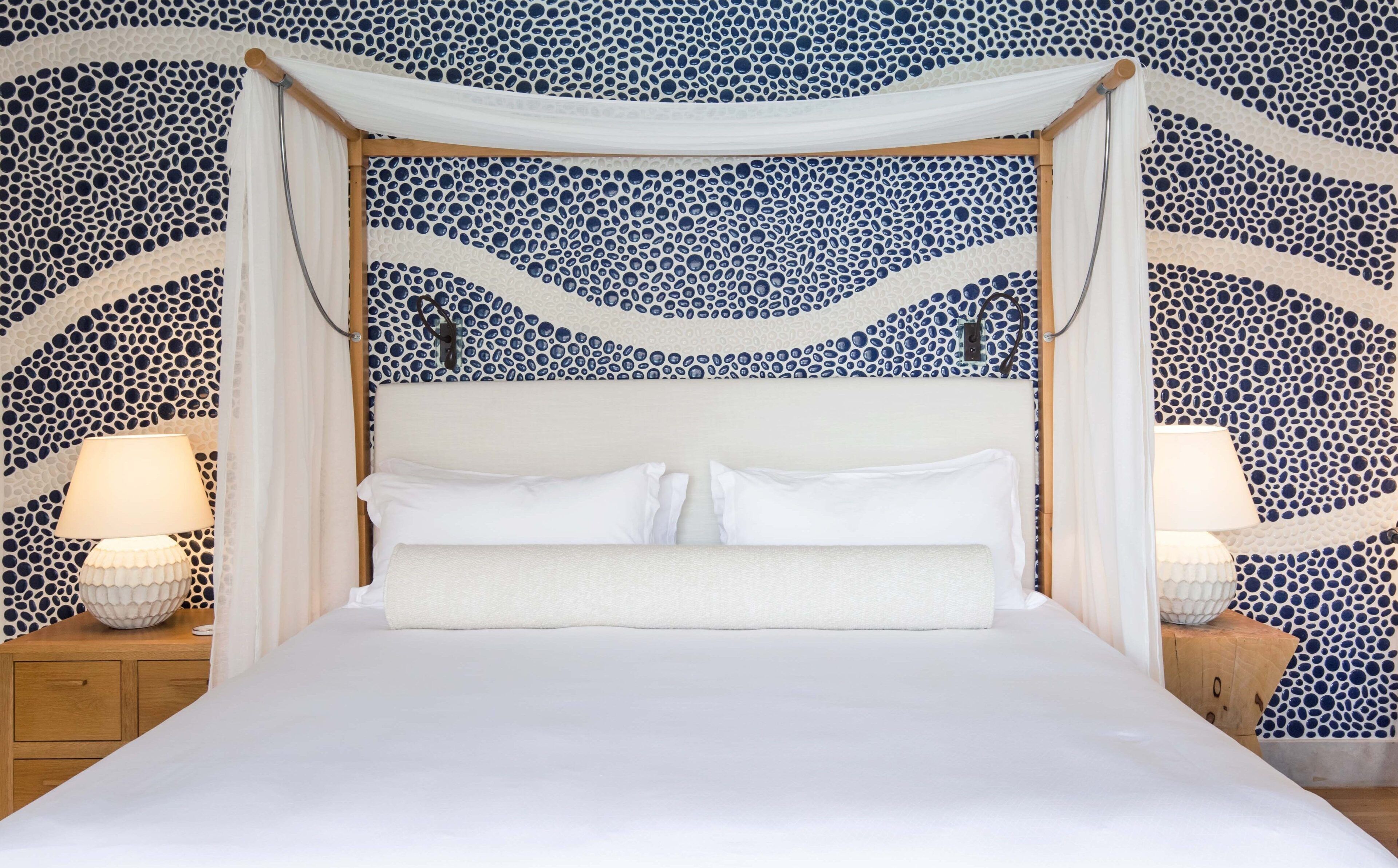 Una cama con dosel, ropa de cama blanca y un papel tapiz estampado.