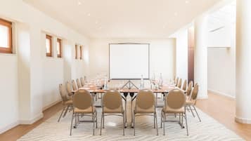 Un salón de conferencias con una larga mesa, varias sillas, una pantalla de proyector y piso alfombrado.