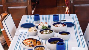 A dining table set with various dishes and blue cups, surrounded by wooden chairs.