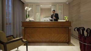 A reception desk with a man standing behind it, a chair to the left, and a row of umbrellas to the right. - Hotel Stendhal (Rome)