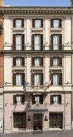 Un edificio de varios pisos con fachada simétrica, ventanas uniformemente distribuidas con contraventanas, una entrada central con toldo y banderas en el segundo piso.