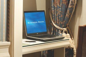 Egy asztalon egy laptop, a képernyőjén a „BUSINESS ROOM” felirattal, egy toll és egy díszítő zsinór található.