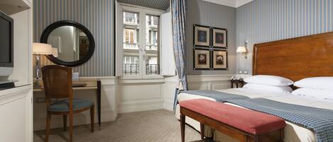 A hotel room with a bed, a desk, a chair, a window with curtains, and framed pictures on the wall.