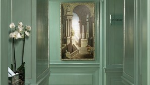 A framed painting of an architectural scene with columns and a staircase, a sign labeled "INTERNET", and a vase with white flowers on a shelf. - Hotel Stendhal (Rome)
