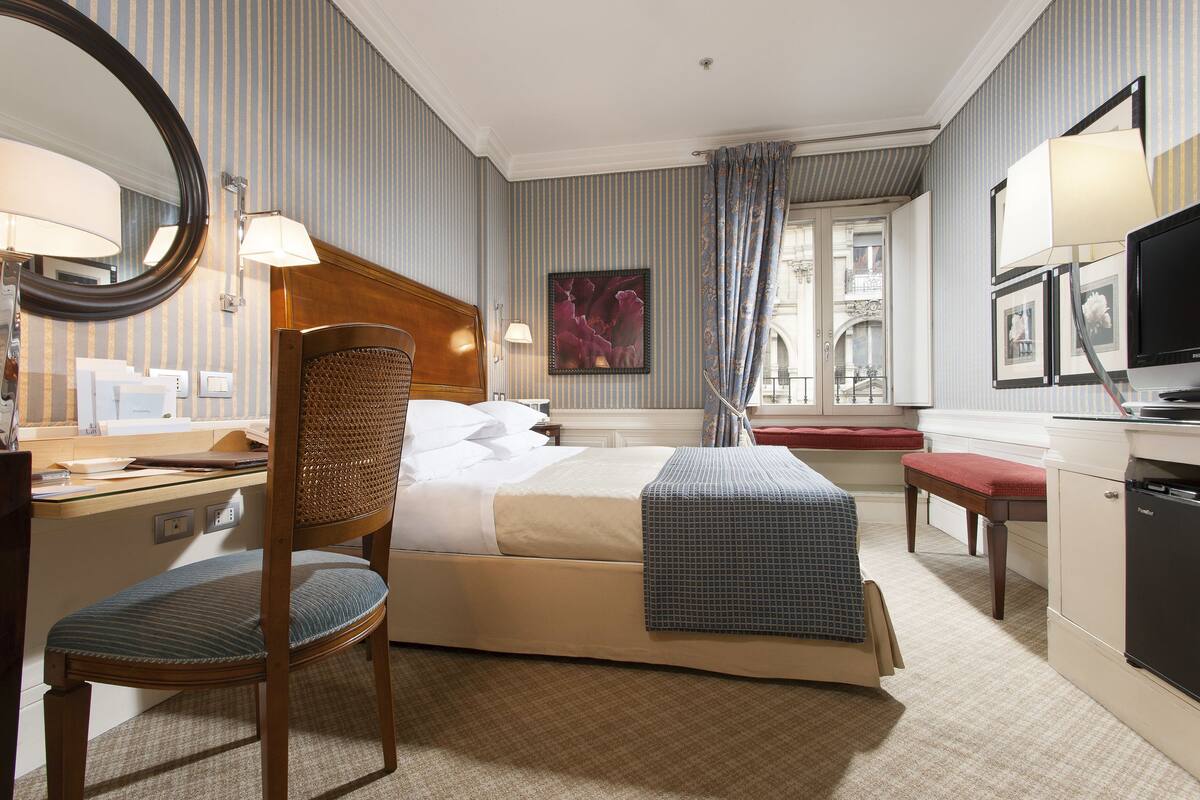 Ein Hotelzimmer mit Bett, Schreibtisch, Stuhl, Fernseher und einem fenster mit Vorhängen.