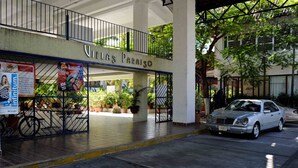 A hotel entrance with a sign reading "Villas Paraiso," a covered area with potted plants, and a parked car.