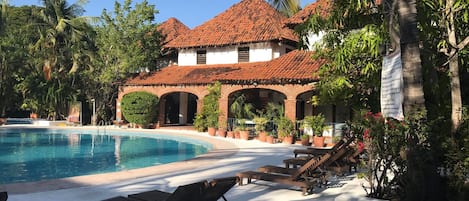 A resort with a swimming pool, lounge chairs, and a building with a red-tiled roof.