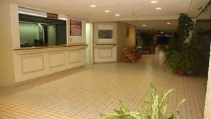 A reception area with a reception desk, a sign indicating 'RECEPTION', and a tiled floor. There are chairs and a potted plant in the background.