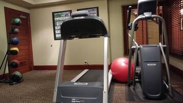 Une salle de sport équipée d’un tapis de course, d’un vélo elliptique et d’un ballon d’exercice rouge.