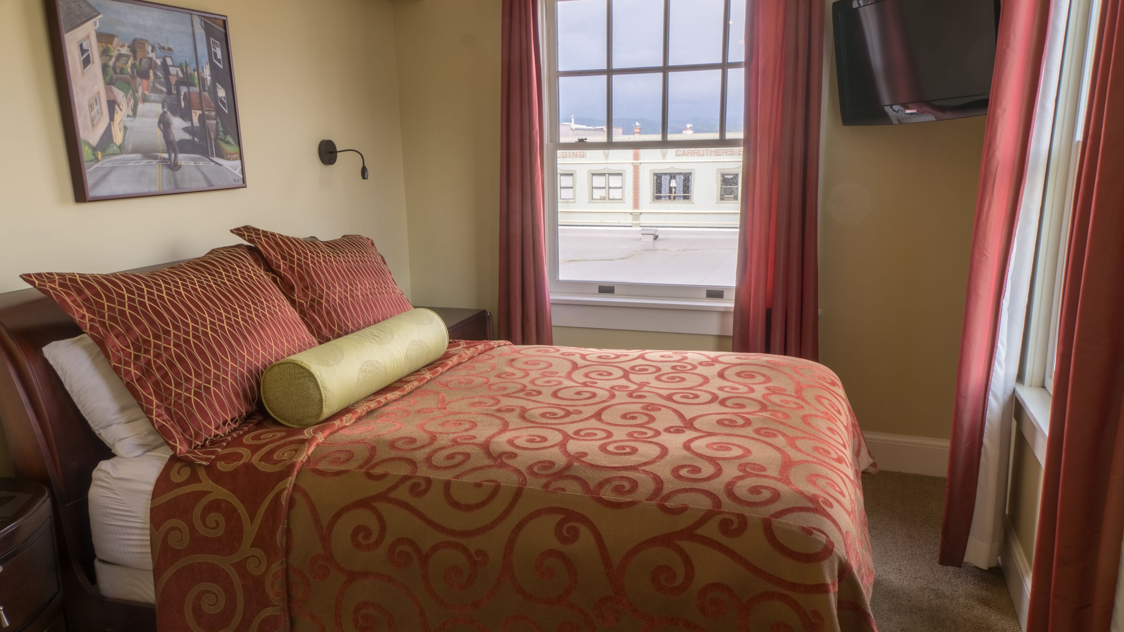 Une chambre d’hôtel avec un lit, un tableau au mur, une fenêtre avec des rideaux et une vue sur la rue.