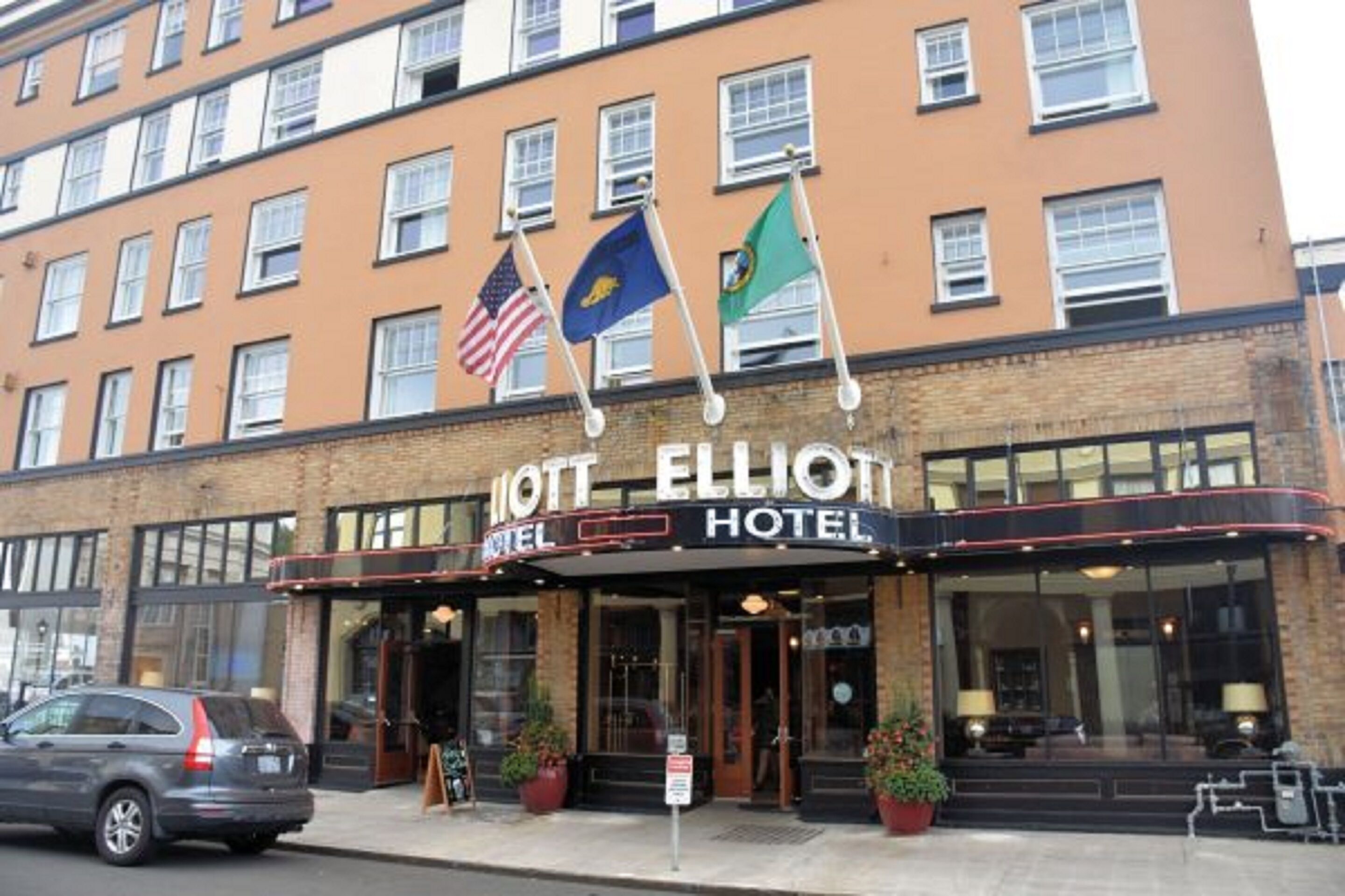 The exterior of the Elliott Hotel with a brick facade, large windows, and a marquee sign.