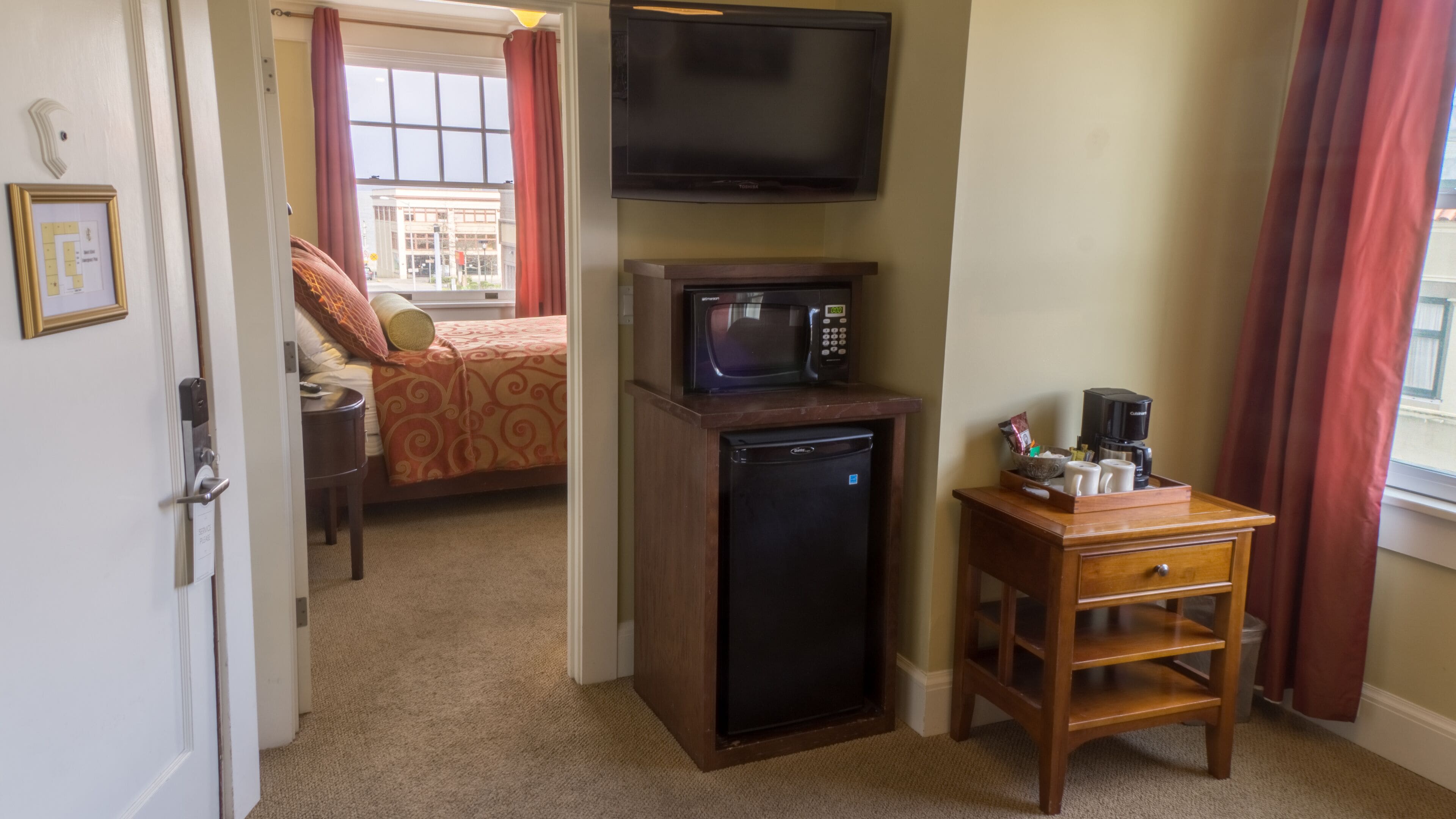 A hotel room with a bed, a TV, a microwave, a coffee maker, and a small wooden side table.