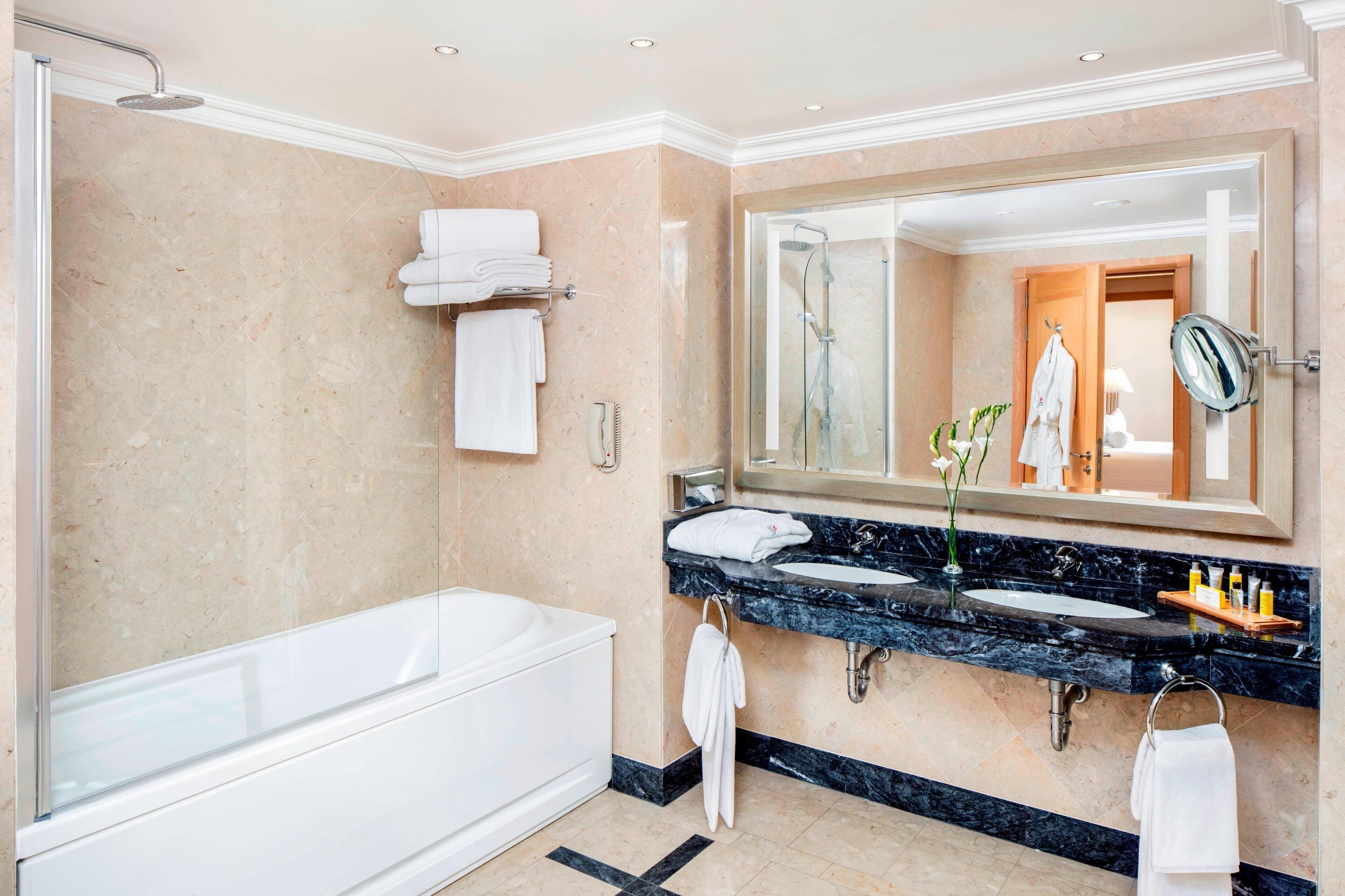 A modern bathroom with a bathtub, two sinks, a large mirror, and a shower.