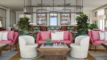 Una sala de estar moderna con una mesa de centro, dos sofás rosados y una zona de bar con estantes llenos de botellas.
