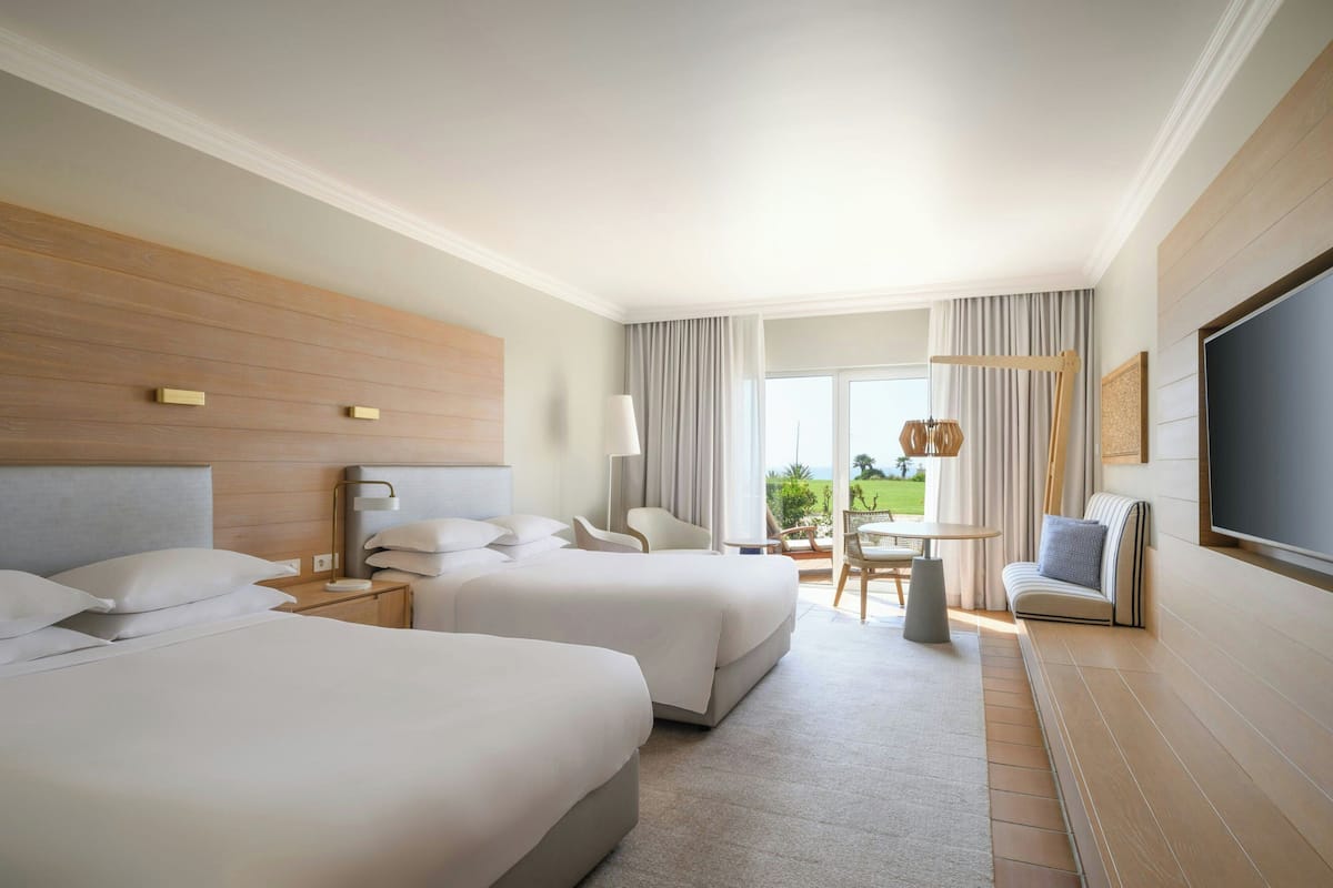 A hotel room with two beds, a sofa, a TV, and a balcony with a view.