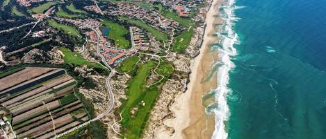An aerial view of a coastal town with a beach, green fields, and residential areas.
