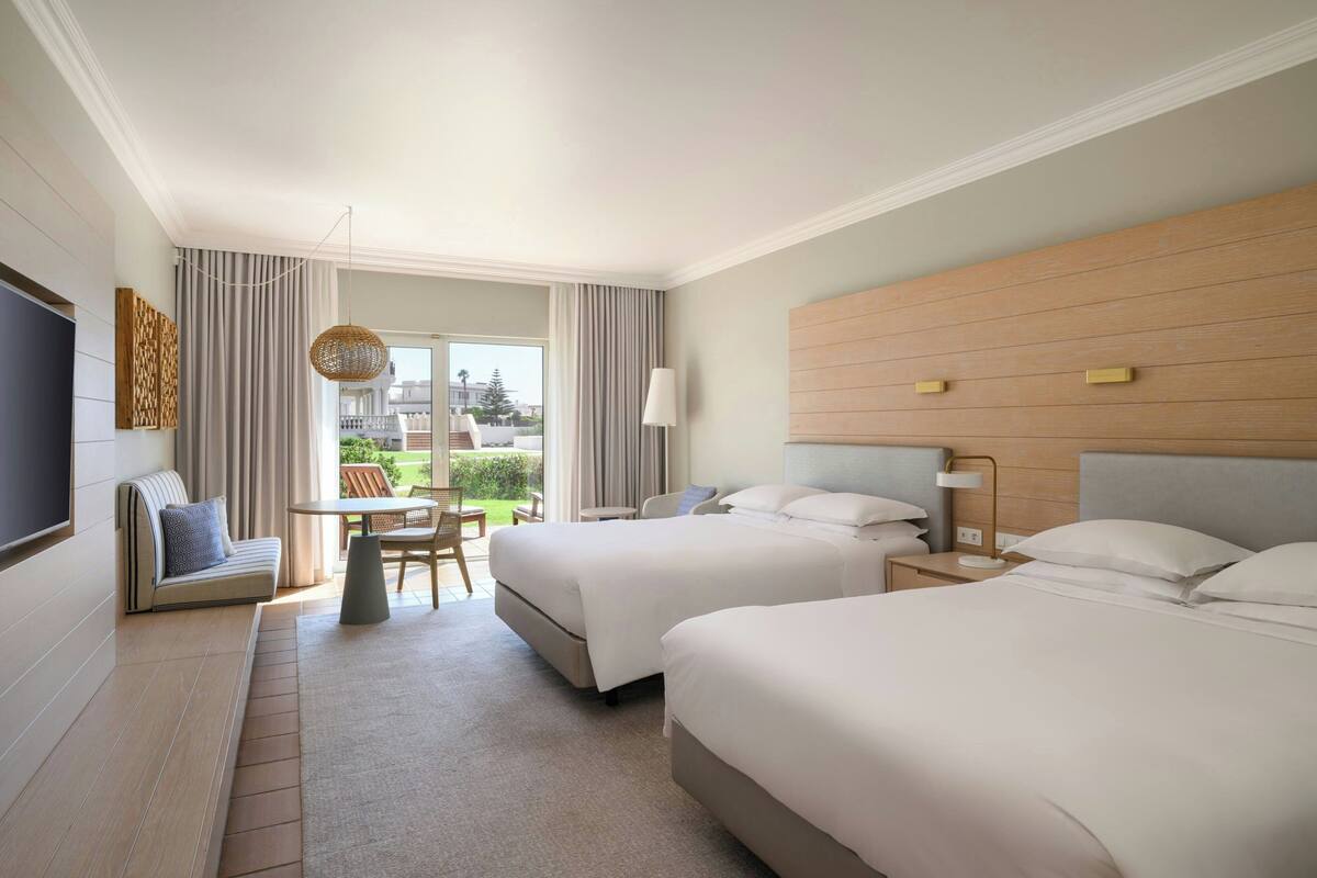 A hotel room with two beds, a sofa, a dining table, and a TV.