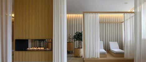 A modern interior with a fireplace, a seating area with a plant, and a room with a bed and curtains.