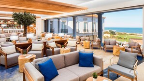A spacious indoor area with multiple seating options, including sofas and chairs, arranged around a central area with a view of the ocean. - Praia D'El Rey Marriott Golf & Beach Resort (Obidos)