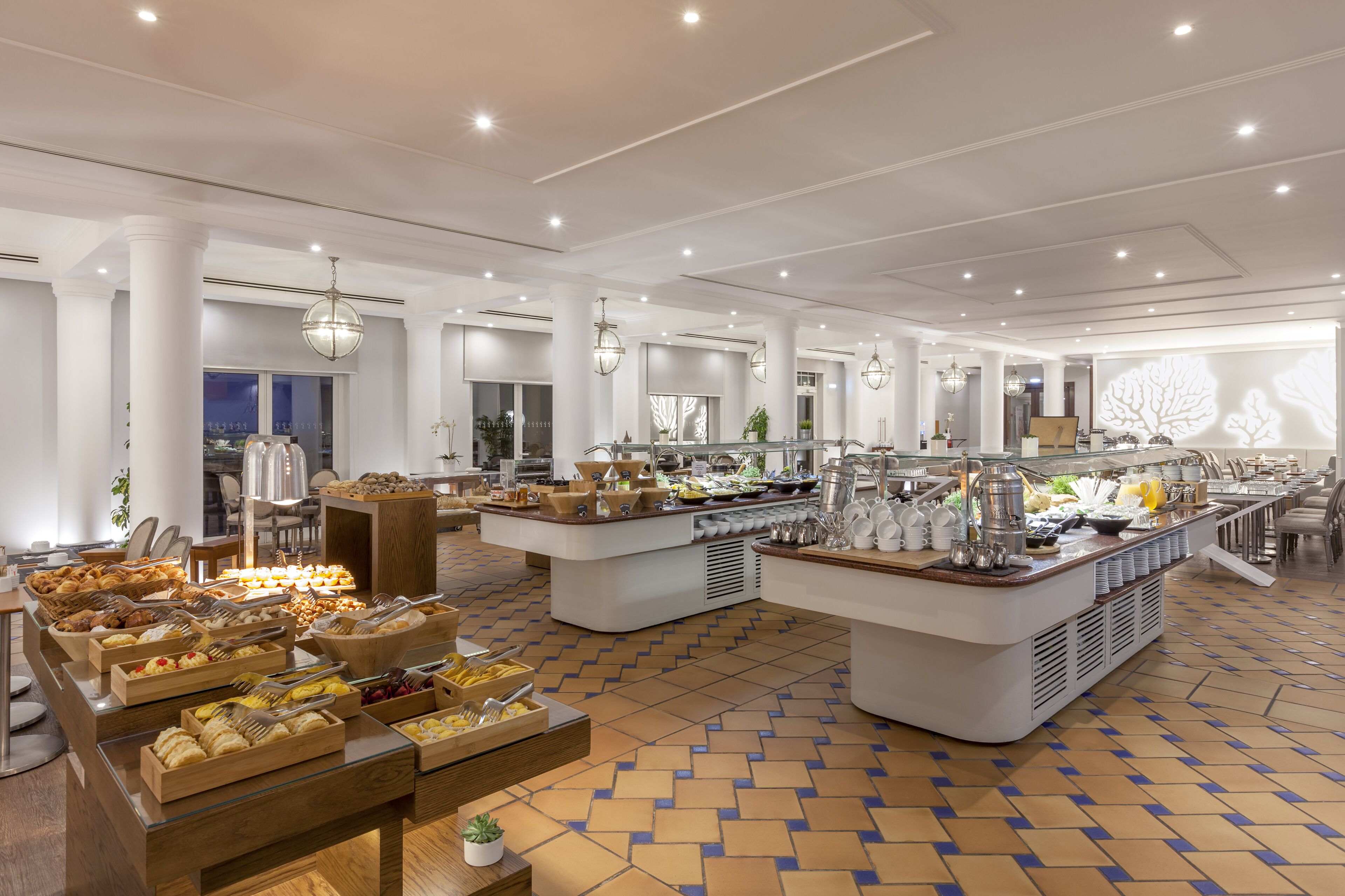 A spacious buffet area with multiple serving stations, a variety of food options, and a tiled floor.