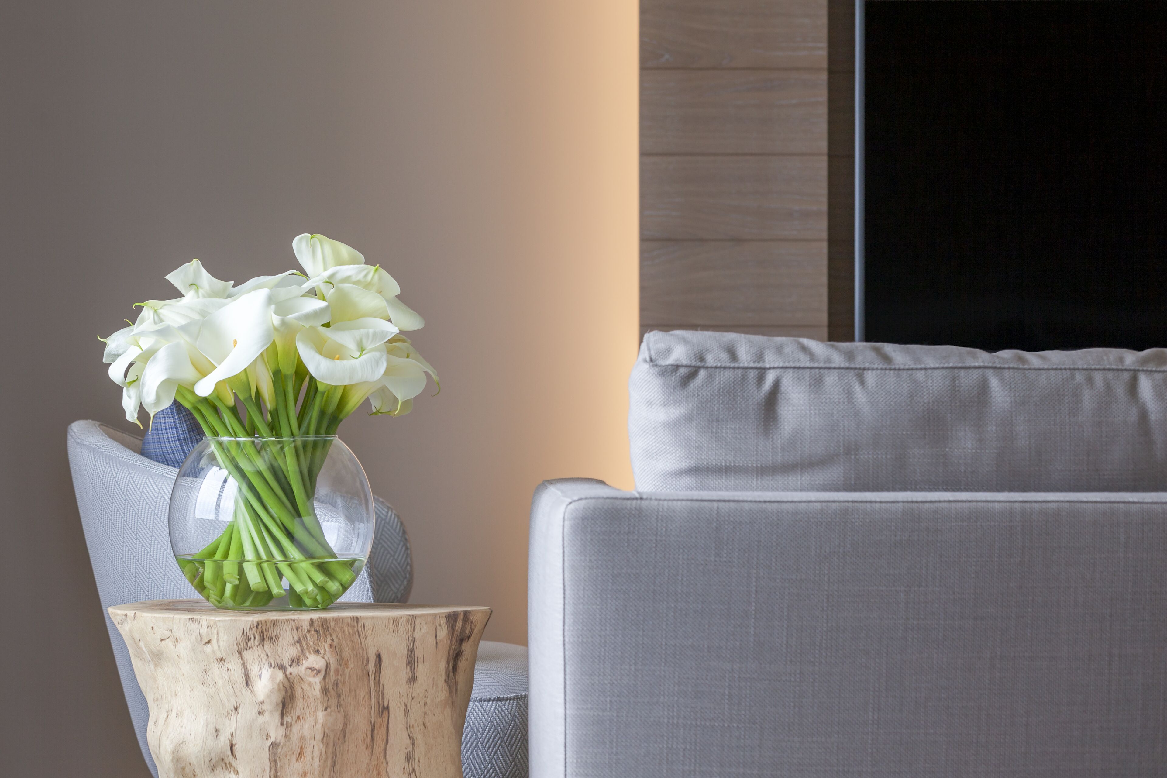 Un salon moderne avec un canapé gris, une table d’appoint en bois et un vase rempli de fleurs blanches.